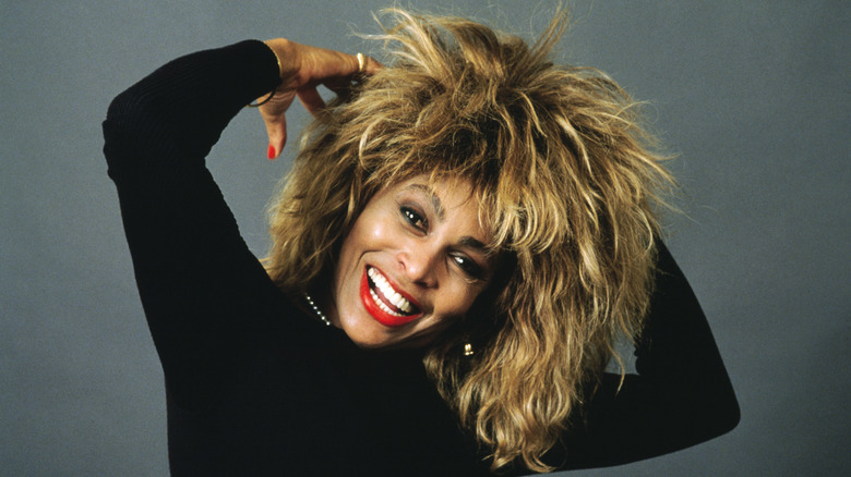 Tina Turner wearing a black shirt and bright red lipstick, smiling for a photo