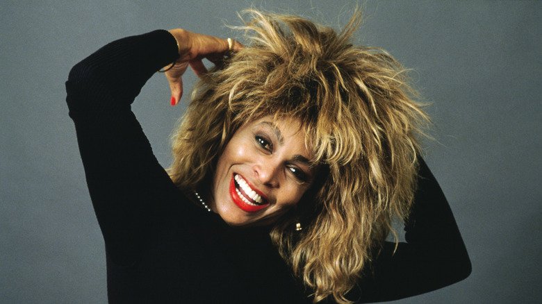 Tina Turner smiling at the camera and tilting her head slightly to the side.