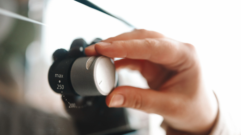 hand adjusting oven temperature with knob