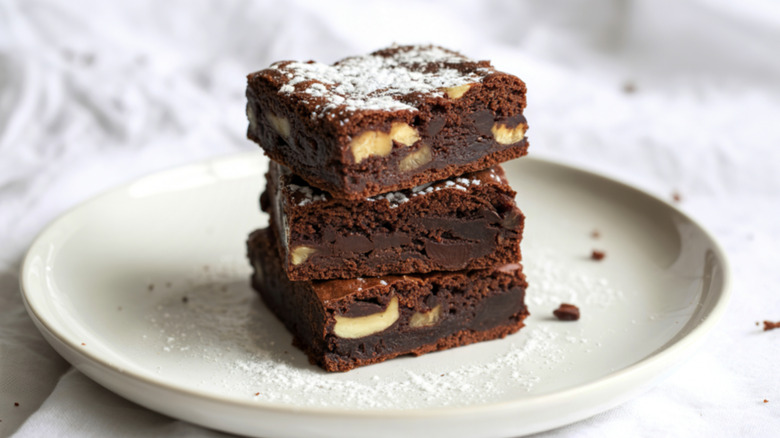 Three brownies with nuts inside stacked on a plate