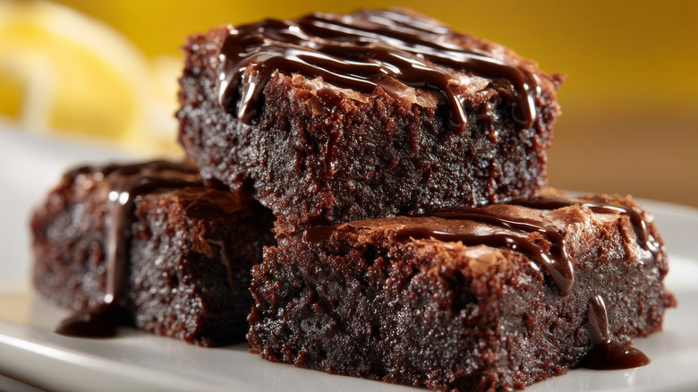 Three brownies on a plate topped with chocolate sauce