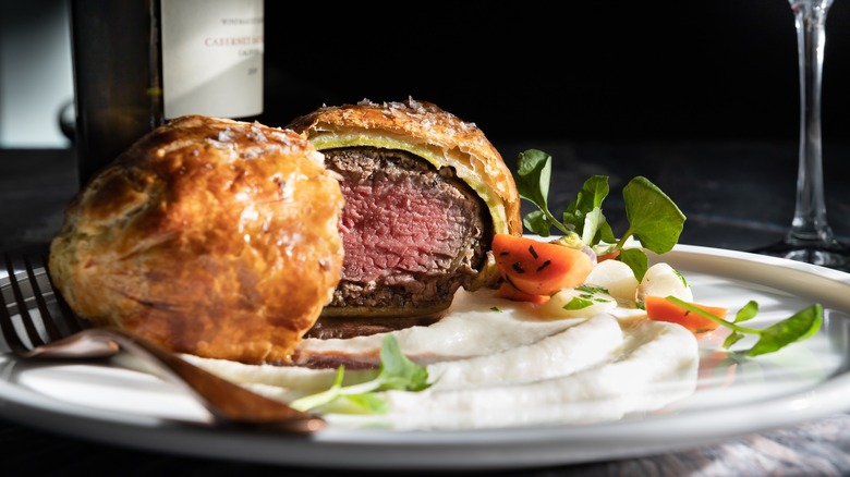 sliced piece of beef Wellington on plate with potatoes and veggies