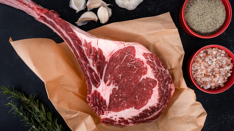 Tomahawk steak on brown paper displayed on a table next to herbs and spices