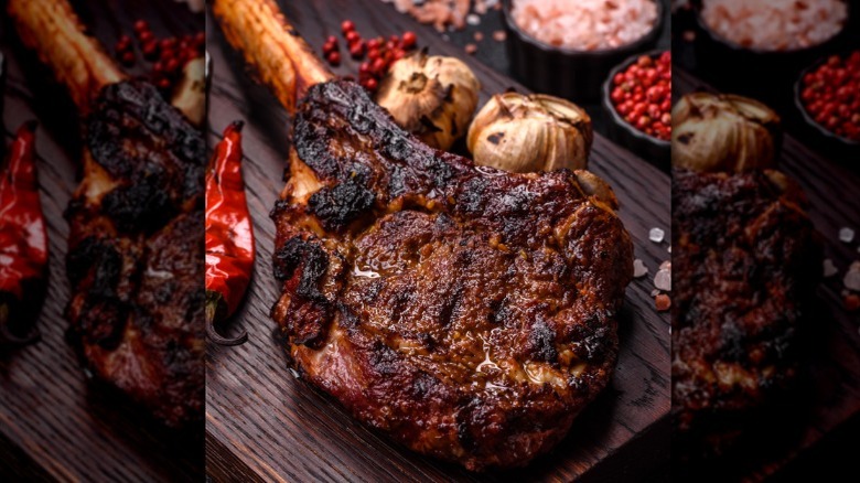 A close-up of a seared tomahawk steak sitting on a wooden surface with other grilled foods