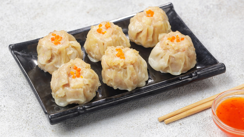 Six shumai sit on a black, rectangular dish.