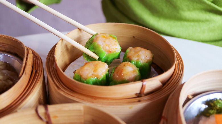 Four green wrapped shumai sit in a steamer basket with chopsticks.