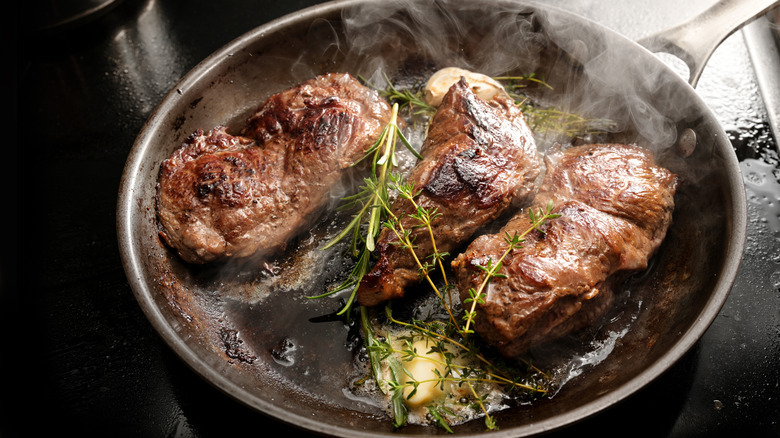 Three seared steaks are sizzling in a pan with butter and rosemary.