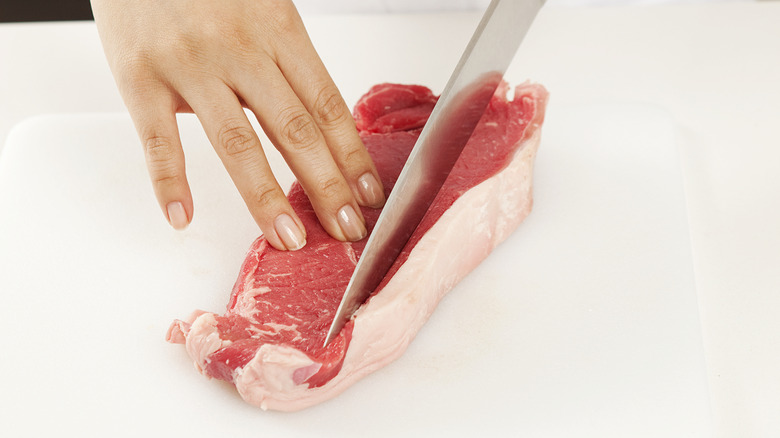 A knife trimming a beef cutlet
