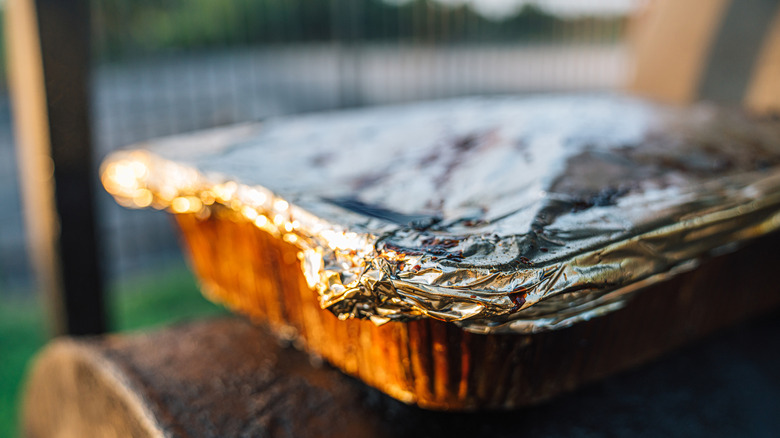 A foil dish covered in foil wrap on top of a smoker