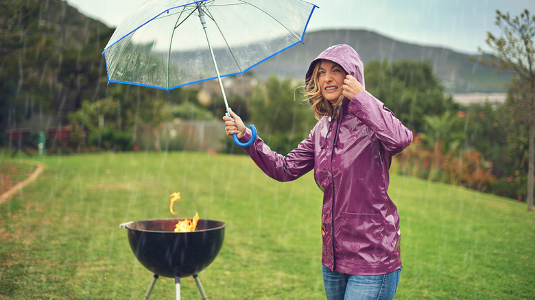 A woman holding an umbrella and grilling in the rain