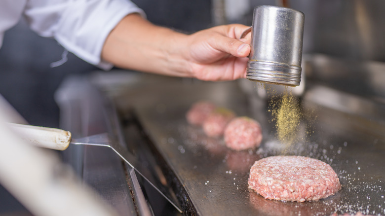 A chef seasoning burger patty