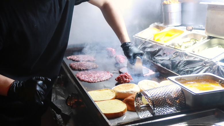 A worker smashing burgers at grill
