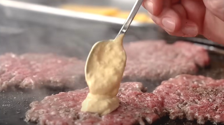 A hand applying sauce onto burger patty
