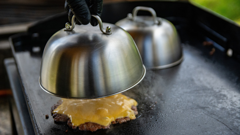 A person covering cheese burger on grill