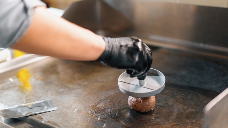 A person smashing a burger on grill