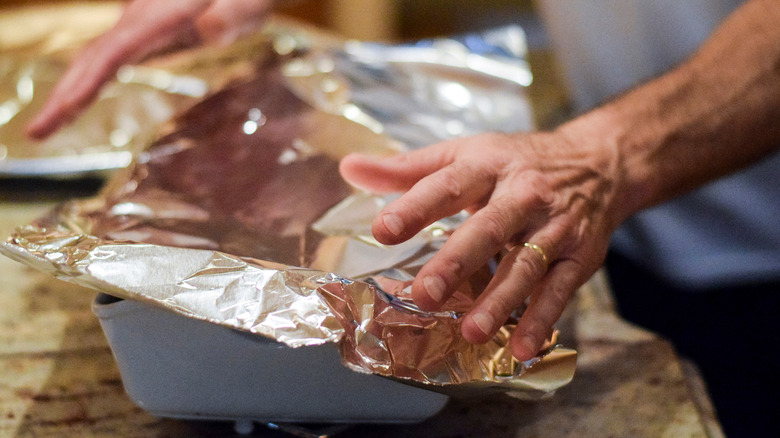 Hands covering a casserole dish with aluminum foil