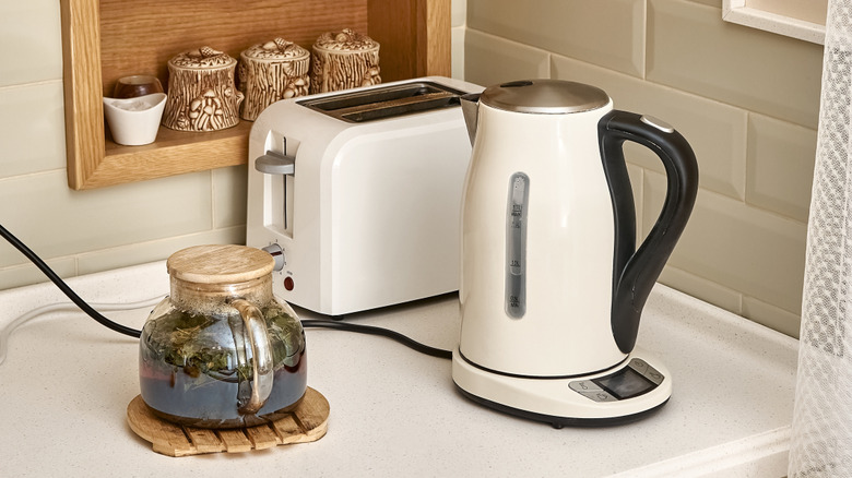 A tea kettle and toaster on a kitchen counter plugged into the wall