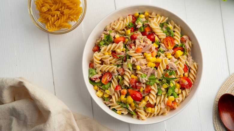 Homemade macaroni salad with trivelle pasta and canned tuna, carrot, Head Lettuce, tomato, corn and mayonnaise dressing in a white plate on wooden table.Top view