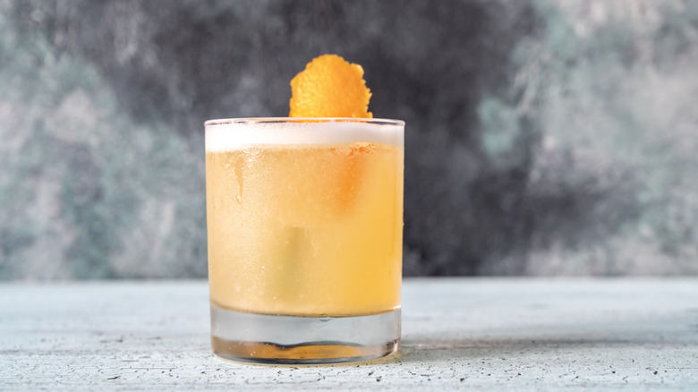 A whiskey sour is garnished with an orange peel.