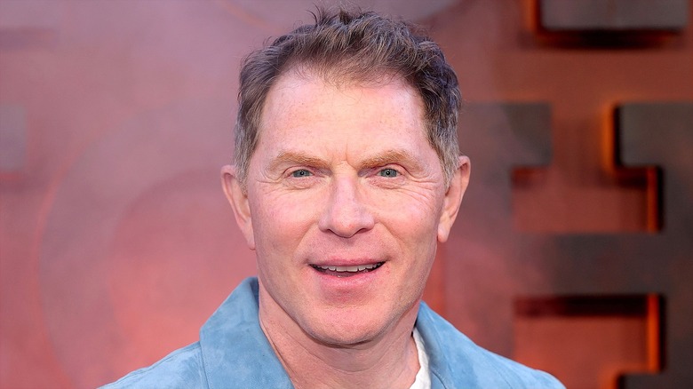 Bobby Flay half-smiling with teeth, wearing a light blue sport jacket over a white shirt.