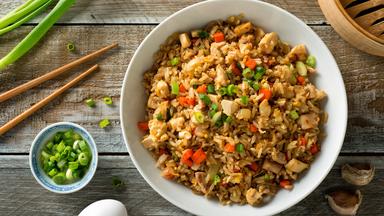 bowl of chicken fried rice in white bowl with scallions and chopsticks beside it on wooden table