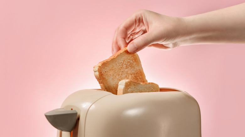 A woman taking out toasted bread from a toaster.