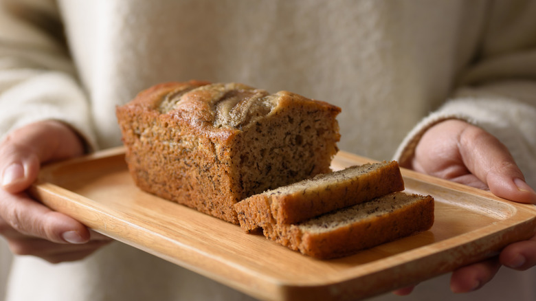 Person holding a wood plate of homemade banana bread.
