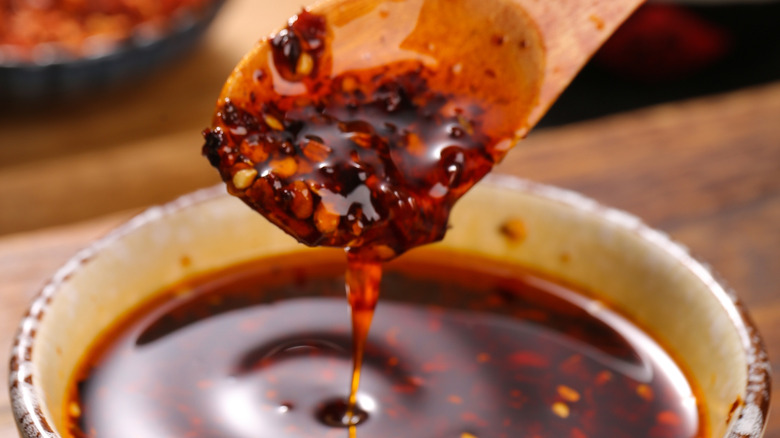 Szechuan chili oil in a small condiment bowl, with a wooden spoon scooping up some of the condiment