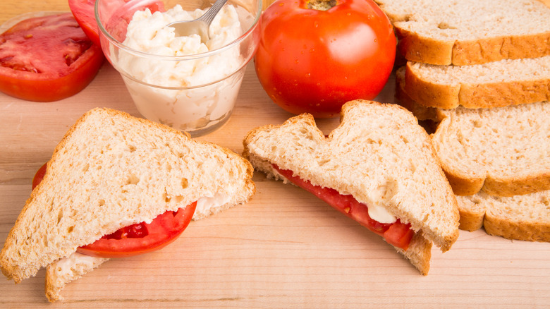 Halved tomato sandwich surrounded by bread, tomato, and dip.