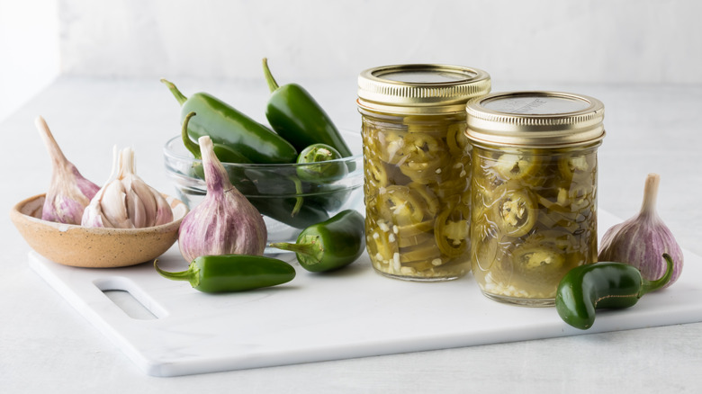 canned pickled jalapenos, fresh jalapenos, and garlic bulbs on cutting board