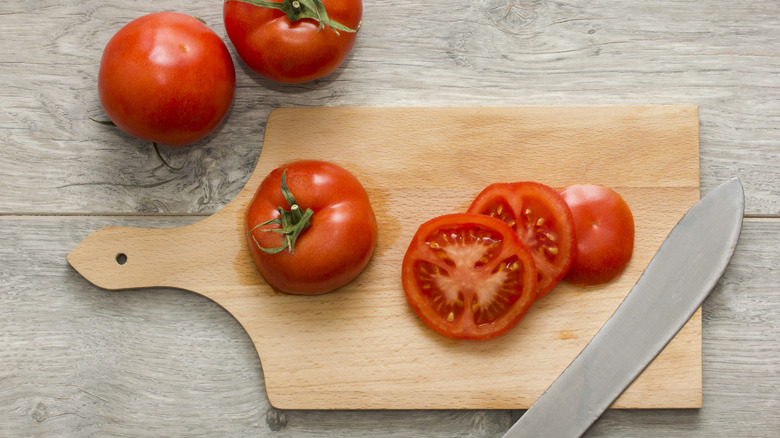 Sliced tomato on wooden kitchen table with a knife on the side.