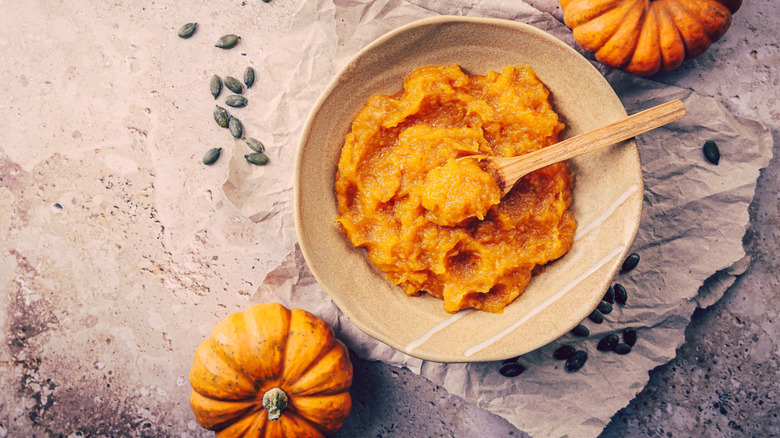 Pumpkin puree in a bowl on a table with small pumpkins beside it