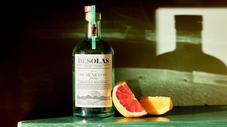 A bottle of Desolas mezcal next to grapefruit and orange slices