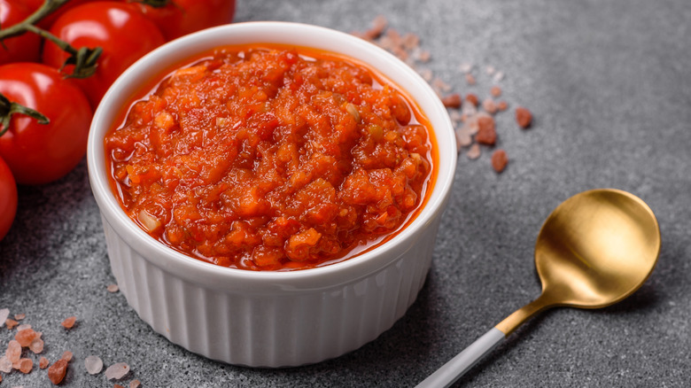 A small white container filled with marinara sauce next to a gold spoon