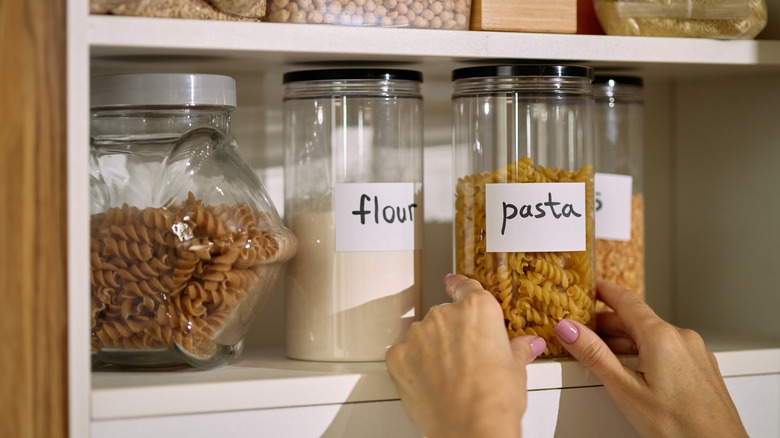 A person's hands are seen arranging labeled glass jars in a small pantry.