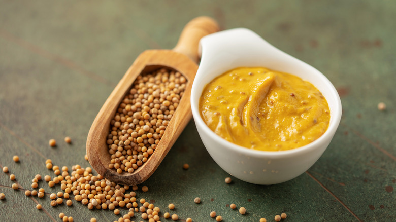 A small pot of mustard beside a scooper full of seeds.