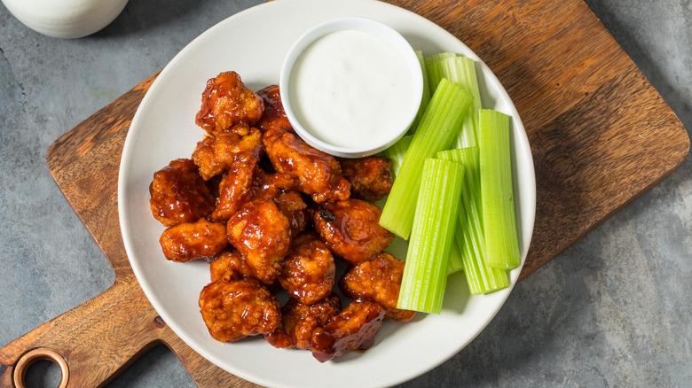 A pile of glazed chicken wings in a plate with celery sticks and a dip