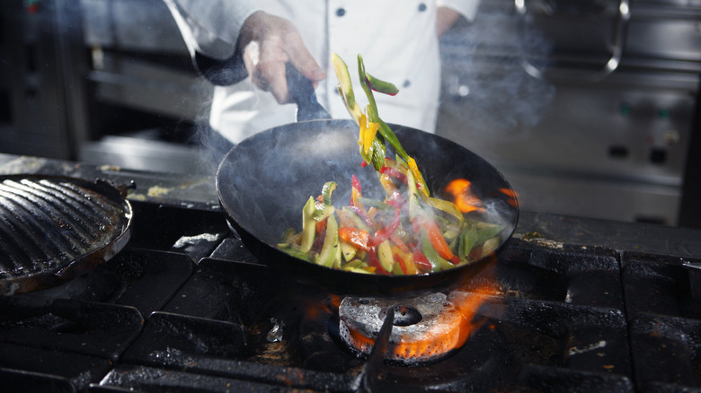 Chef tossing vegetables in a pan over a flame