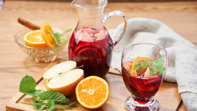 A pitcher and glass of sangria on a table with fruit