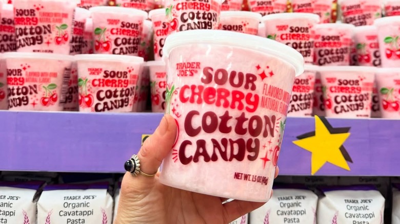 A hand holds a tub of Sour Cherry Cotton Candy against a backdrop display at Trader Joe's