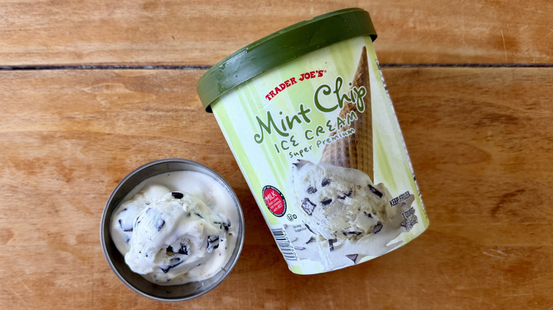 Mint chip ice cream in stainless steel dish next to its container on a wooden table