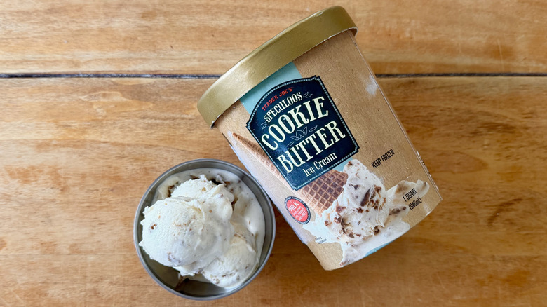 Speculoos cookie butter ice cream in stainless steel dish next to its container on a wooden table