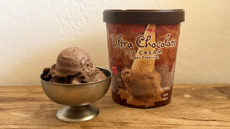 Ultra chocolate ice cream in stainless steel dish next to its container on a wooden table