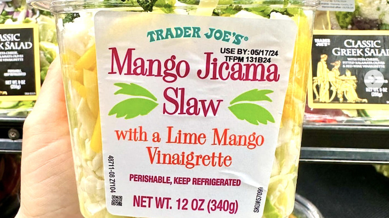 Someone holds a container of Trader Joe's Mango Jicama Slaw