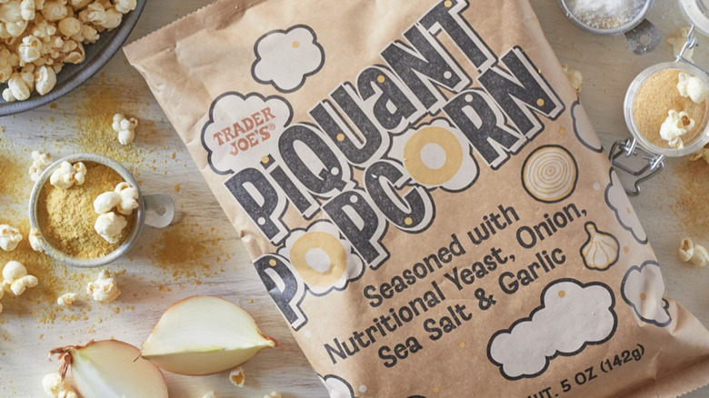 A closed package of Trader Joe's Piquant Popcorn surrounded by cooked popcorn