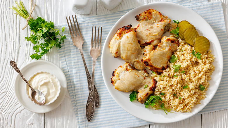 A plate of chicken thighs with rice, tangy pickles, and a dip on the side