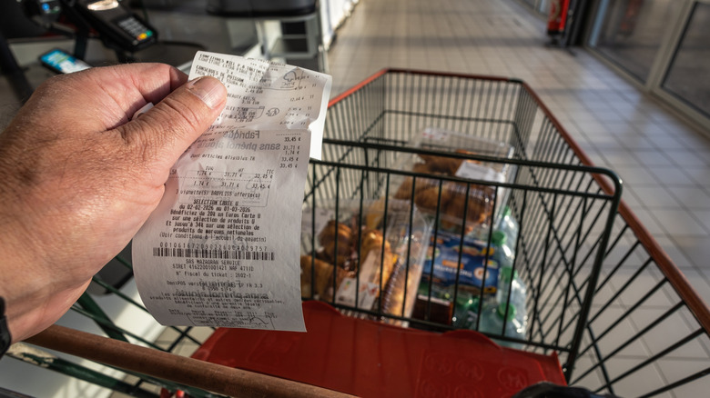 Hand holding receipt while pushing shopping cart in grocery store
