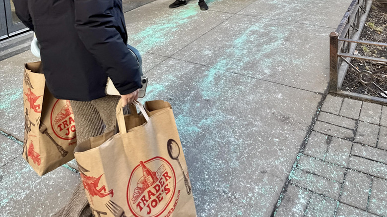 Person holding Trader Joe's grocery bags and walking down sidewalk in the winter