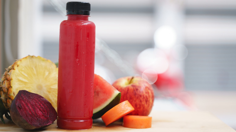 Bottle of red cold-pressed juice on a windowsill surrounded by fresh fruits