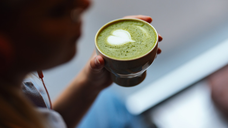 Close up of an unrecognizable person holding a cup of matcha tea with green foam. Replacing coffee with a healthy matcha.